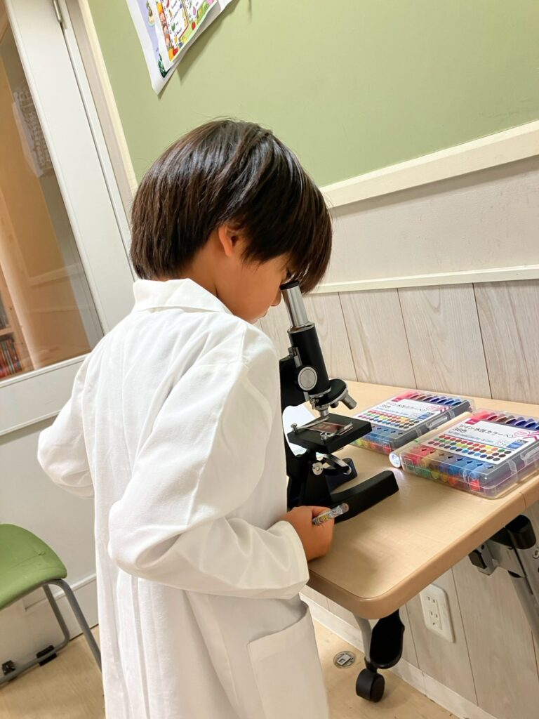 サマースクールで小学生が顕微鏡を使い研究している様子